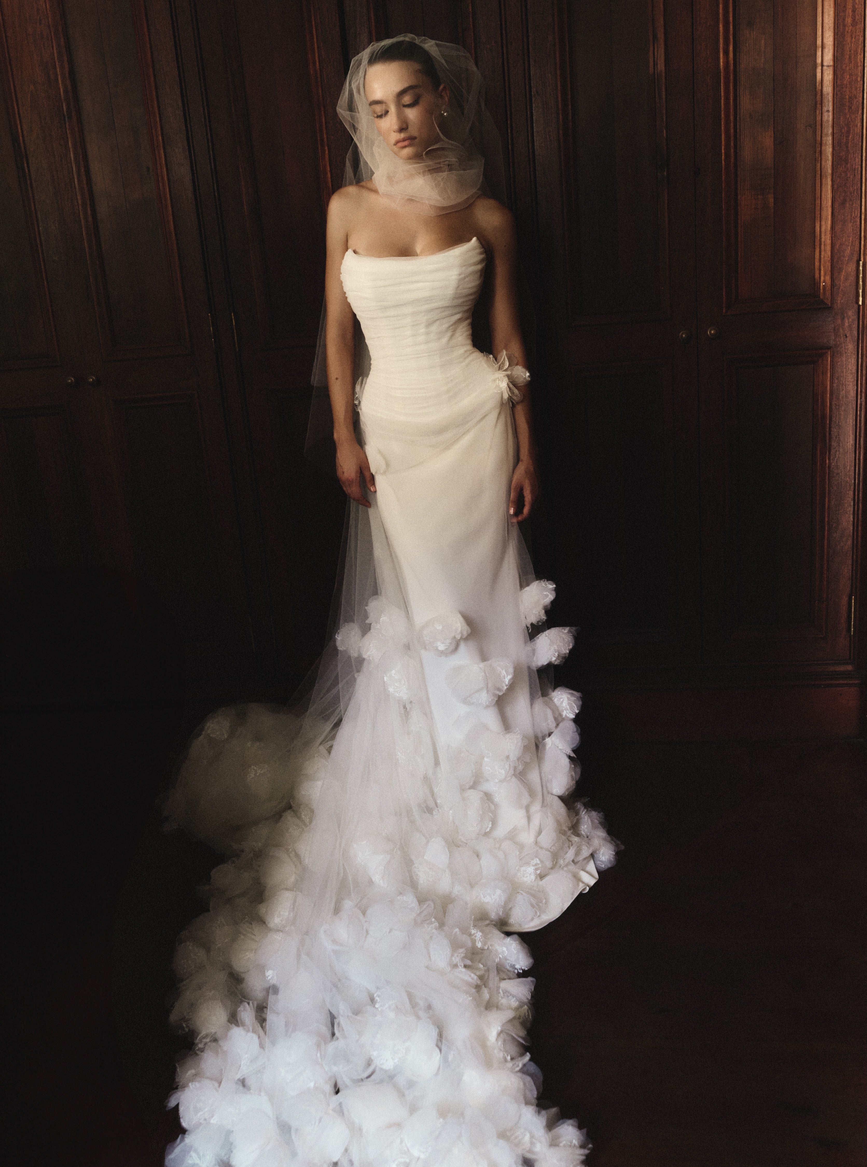 Woman wearing a white wedding dress with a veil and floral details against a dark background