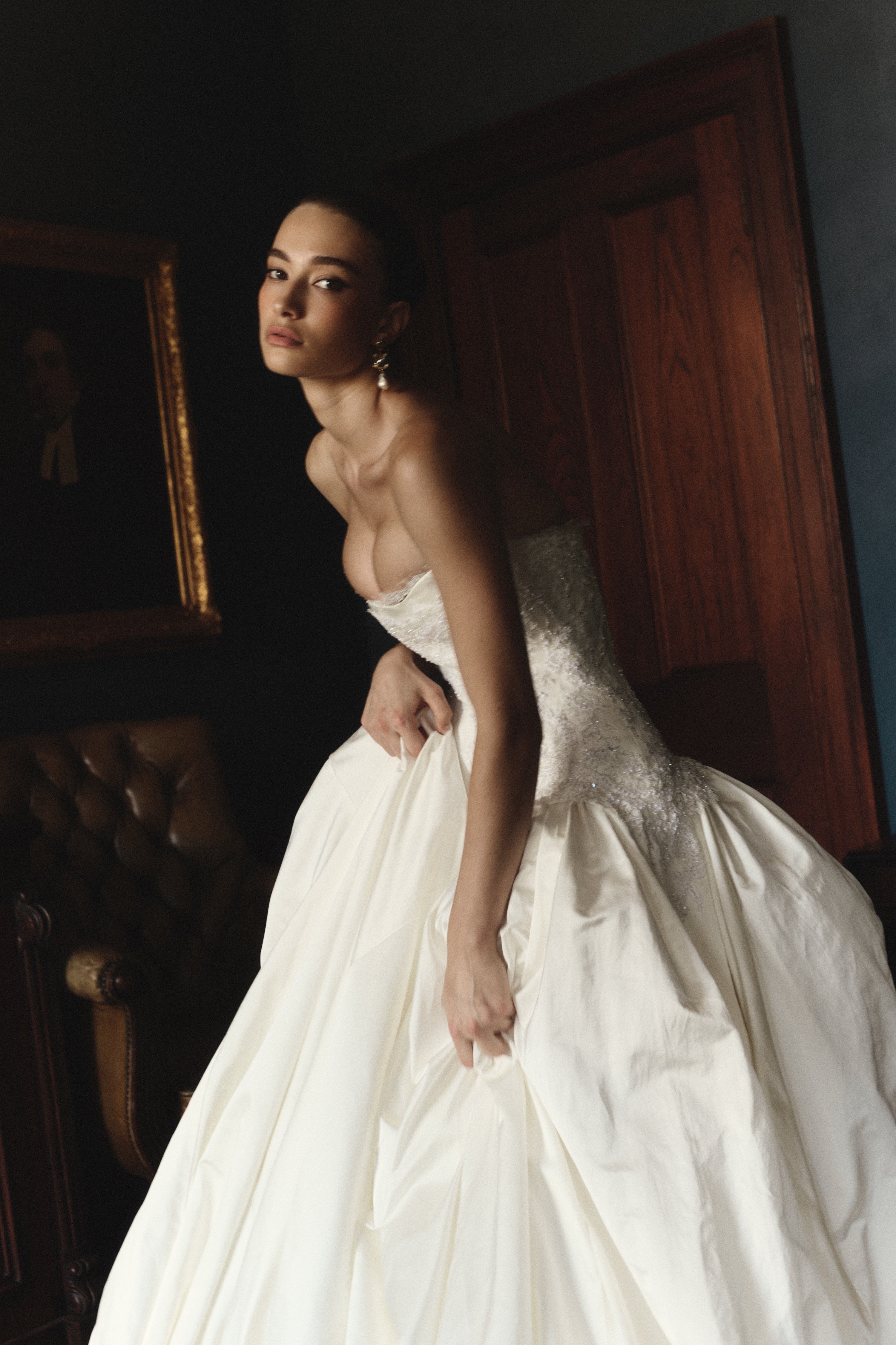 Woman in a white wedding dress standing in a room with a painting in the background